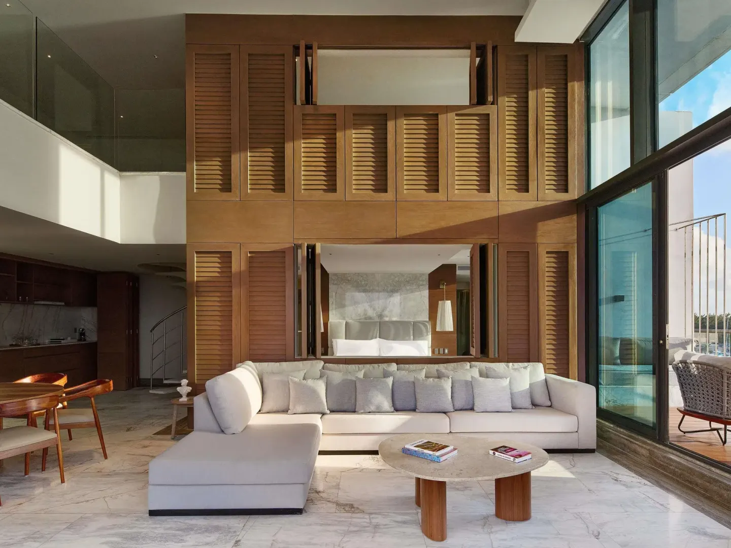 Suite lounge with sectional sofa, wood shutters, dining area, and balcony doors at SLS Playa Mujeres.