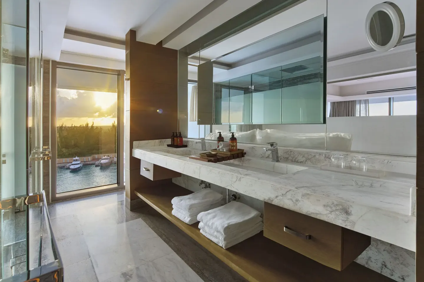 Bathroom with marble vanity, glass shower, towels, and water view in a suite at SLS Playa Mujeres.
