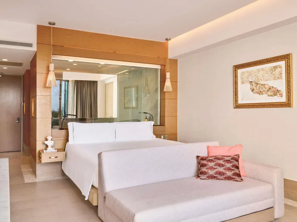 SLS Playa Mujeres bedroom with king bed, sofa, and glass-walled bath at SLS Playa Mujeres.