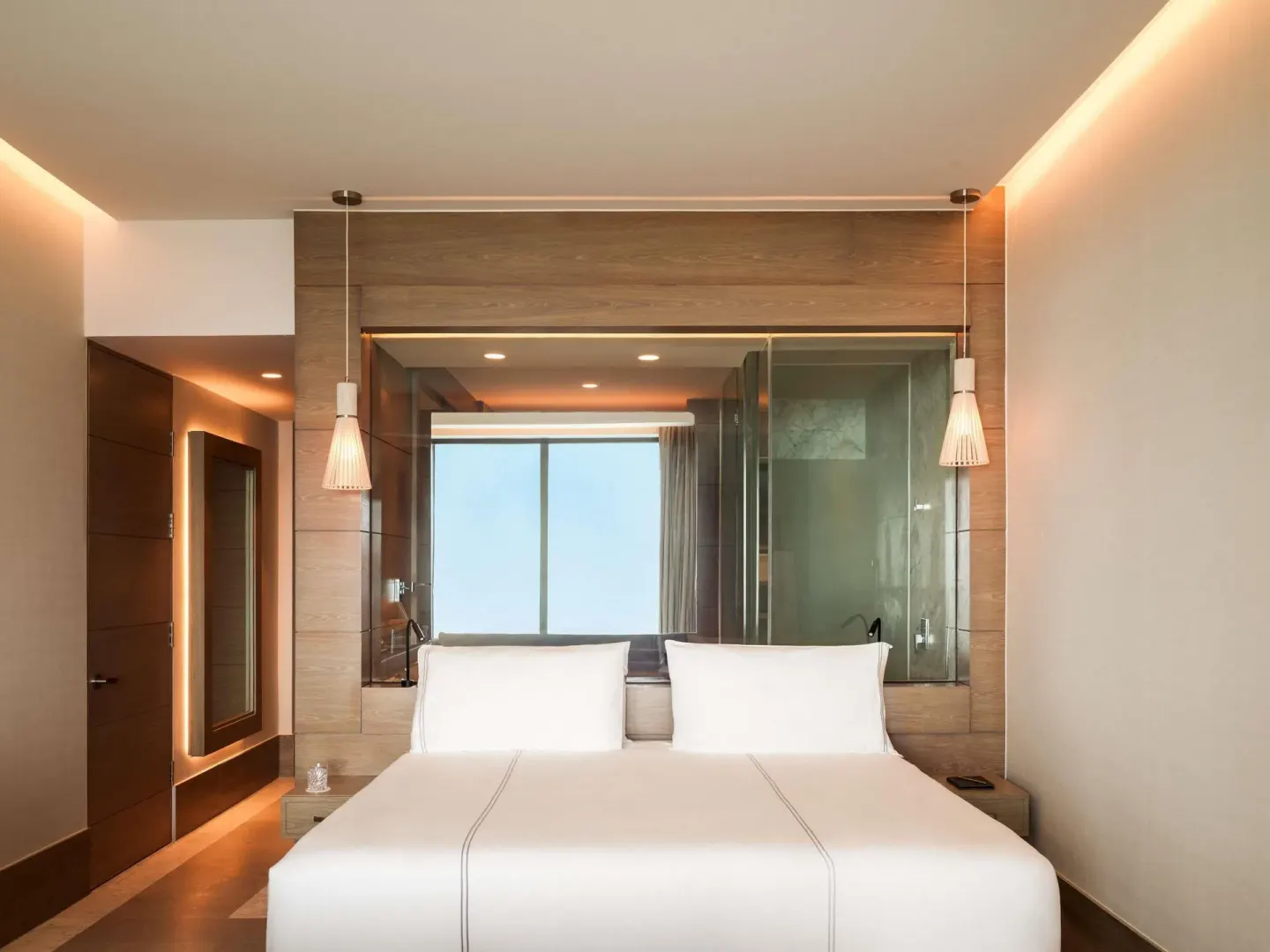 SLS Playa Mujeres king bed at SLS Playa Mujeres with pendant lights and glass-walled bathroom behind.