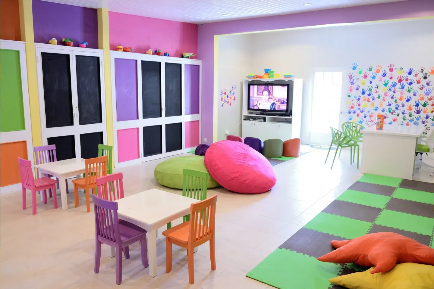 Bright children's playroom with small tables, beanbags and a TV at Spice Island Beach Resort.