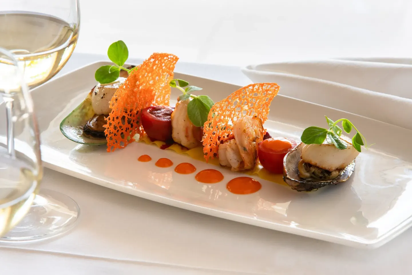 Plated seafood dish with garnishes and wine glasses at Spice Island Beach Resort.