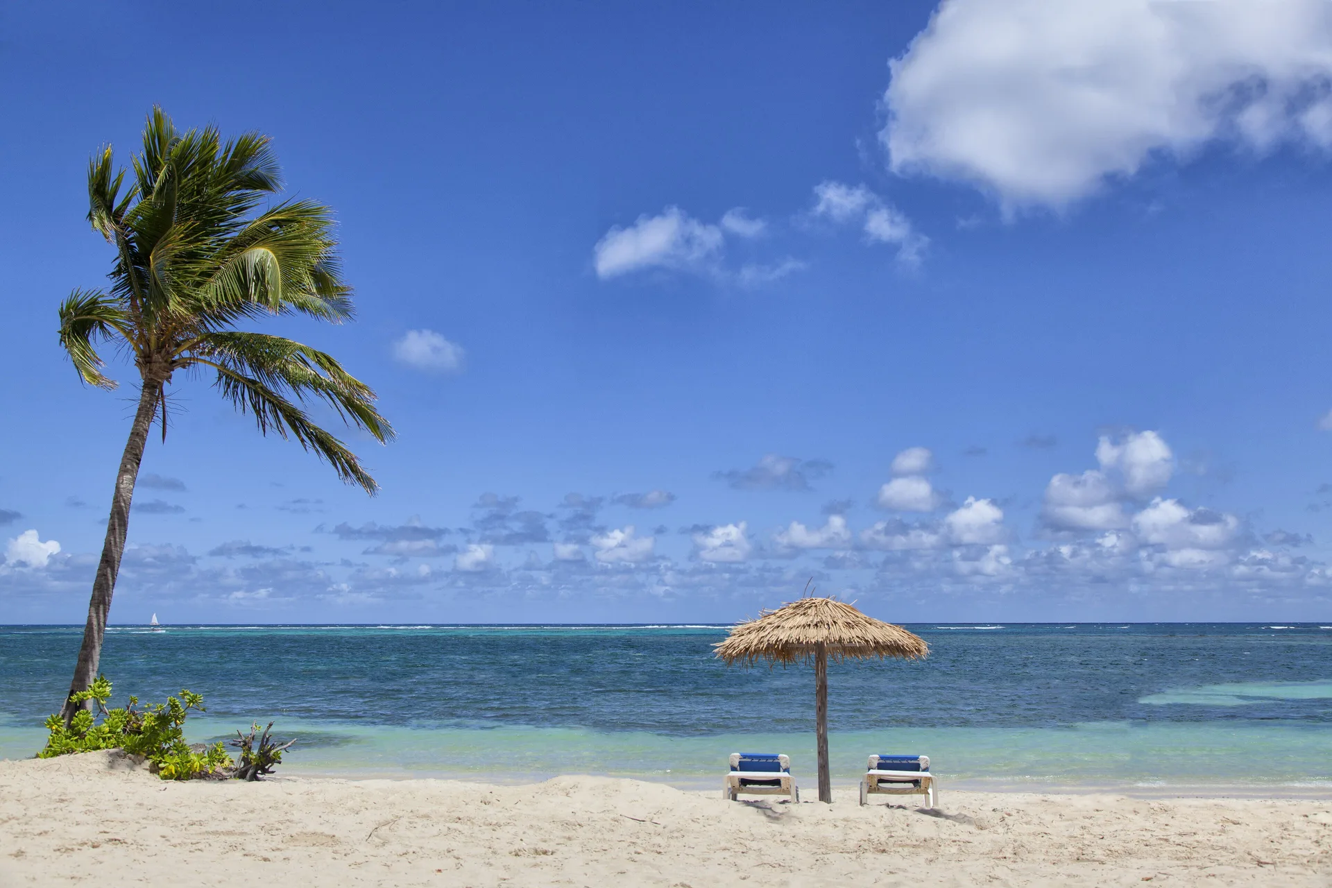 Two loungers under a thatched umbrella facing the sea at St. James's Club Antigua.