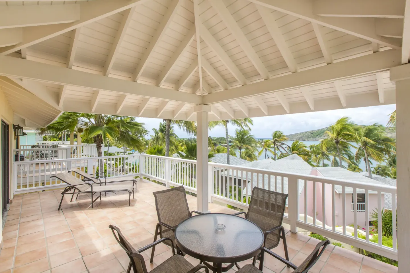 Covered balcony with table, loungers, palms, and water view at St. James's Club Antigua.