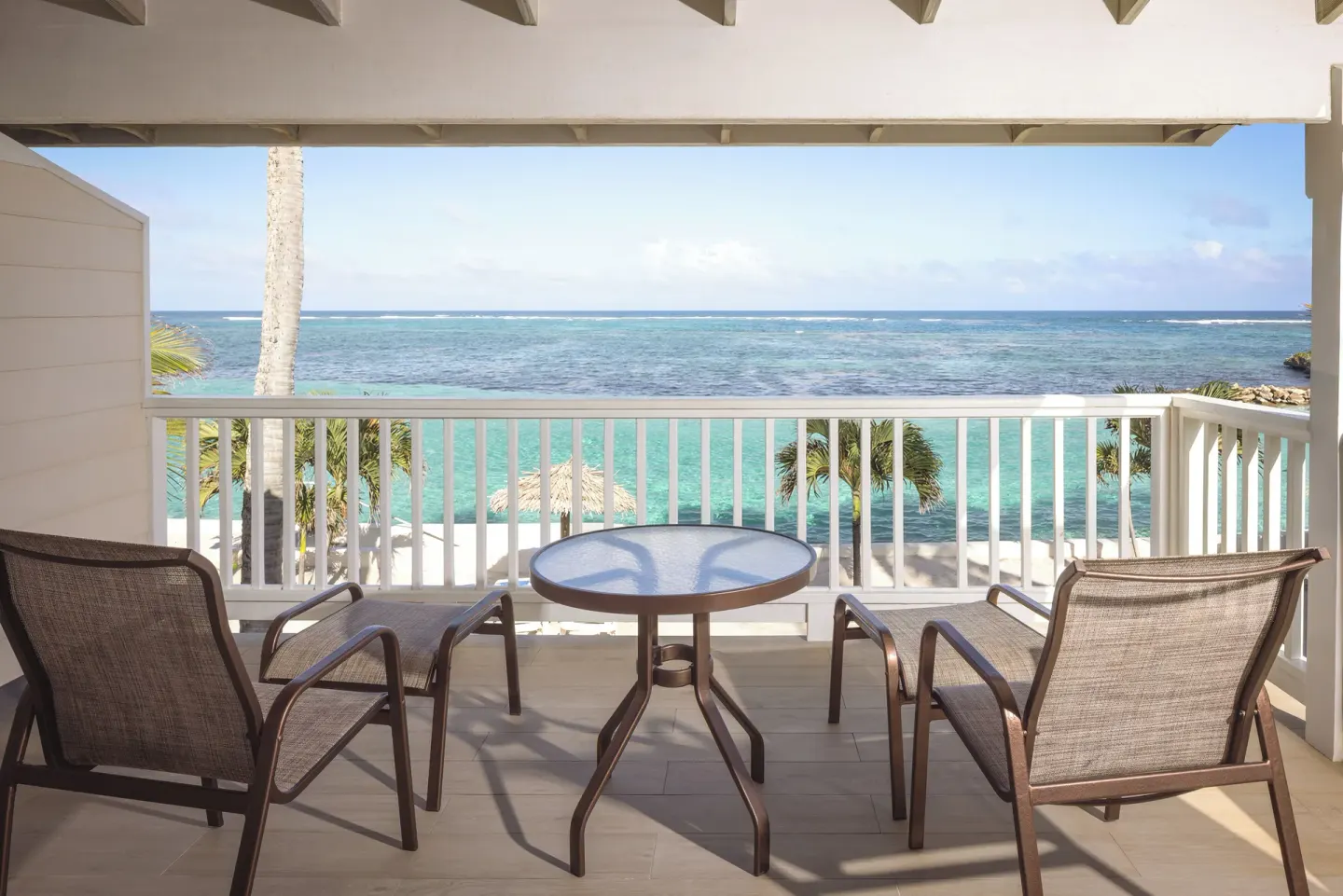 Beachfront Room balcony with chairs, table, and ocean view at St. James's Club Antigua.