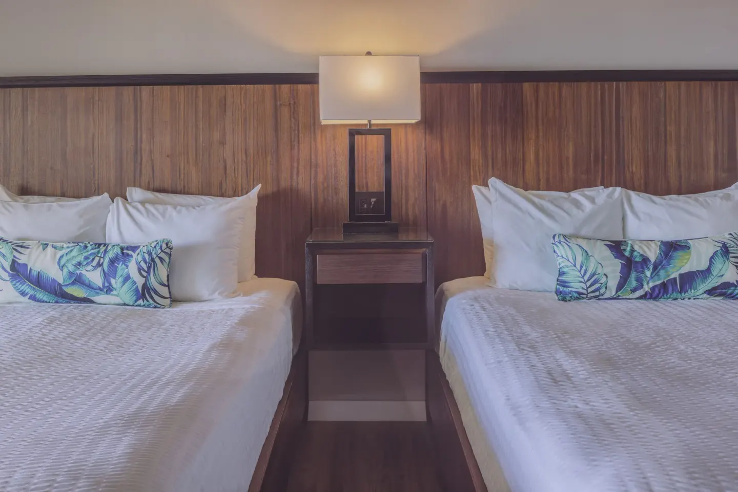 Two beds with white linens and tropical pillows at St. James's Club Antigua.