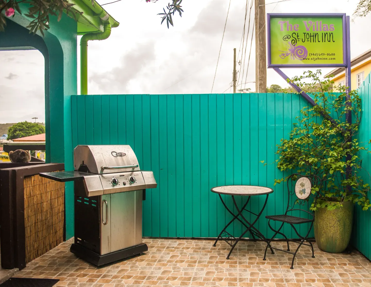 Patio with grill, small table, and St John Inn sign above a teal fence.