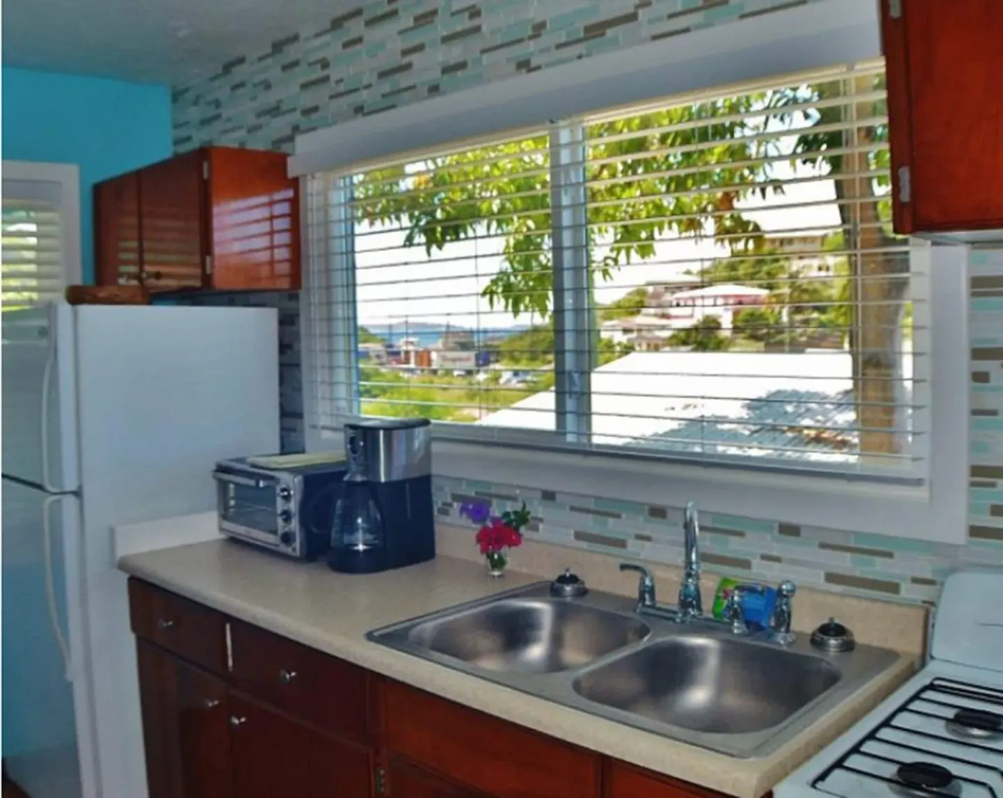 Kitchen counter with double sink, refrigerator, stove edge, and window blinds at St John Inn.