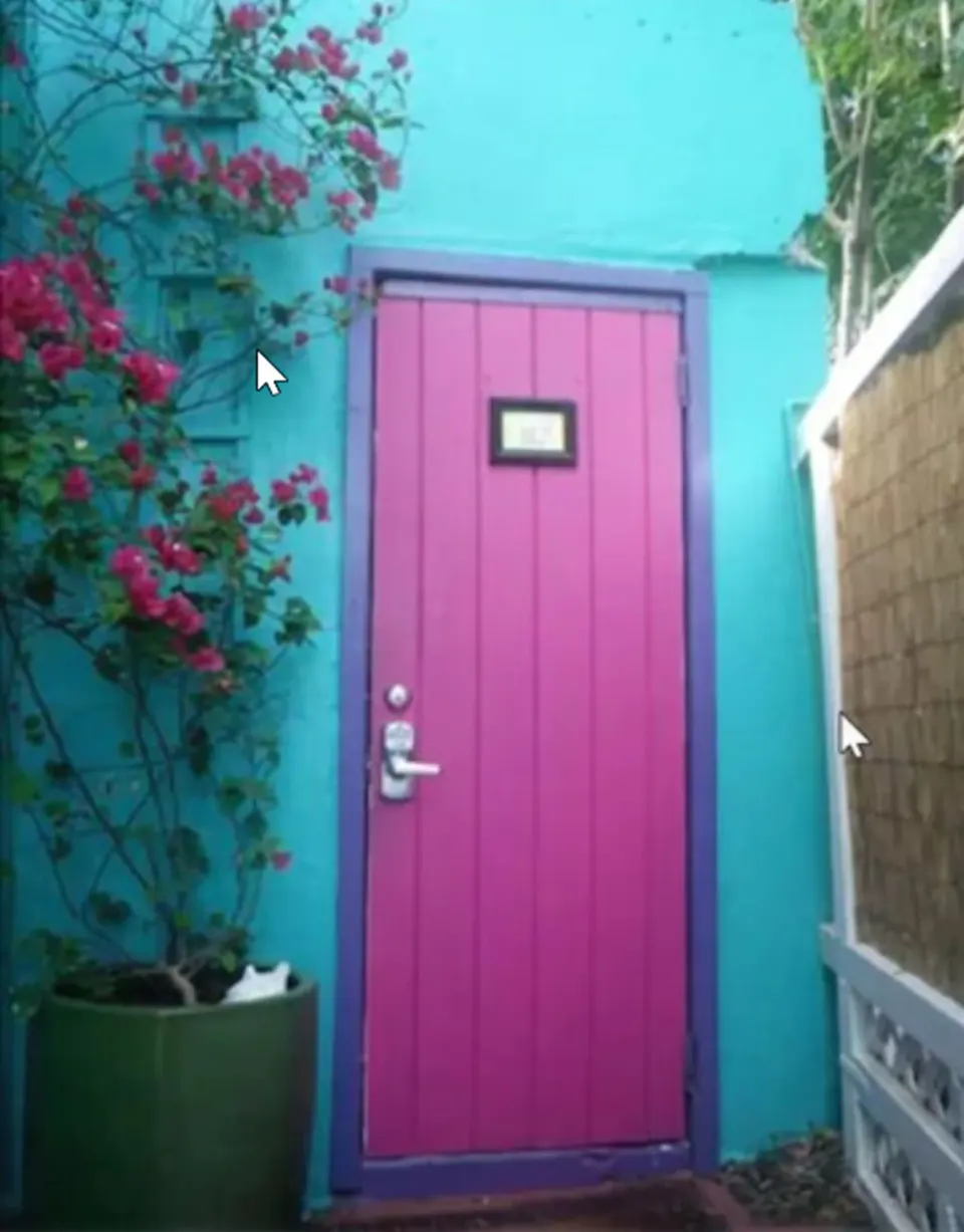 Pink door with purple trim beside flowering plants on a turquoise wall at St John Inn.