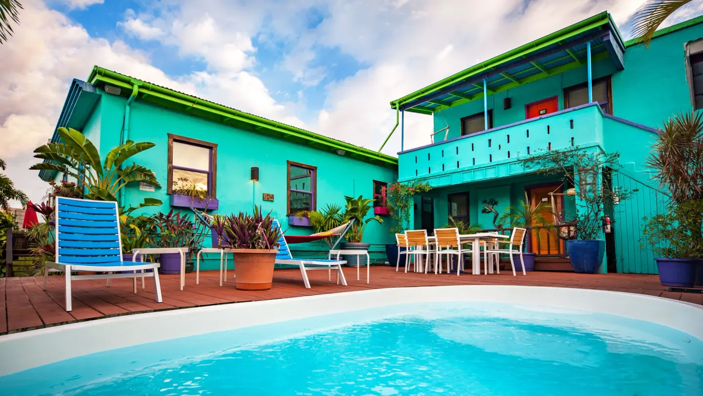 Pool deck with turquoise buildings, loungers, and patio tables at St John Inn.
