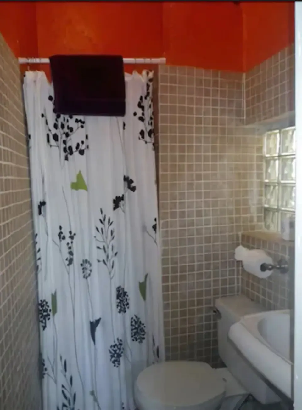 Tiled bathroom with floral shower curtain and orange ceiling at St John Inn.