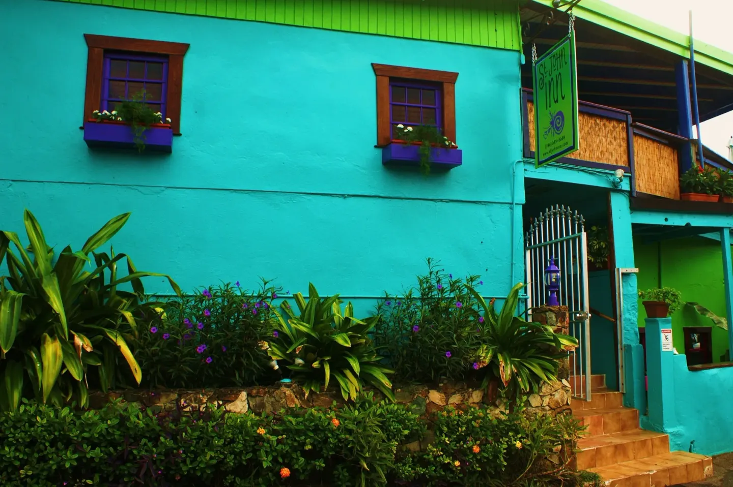 Turquoise exterior with stairs, garden beds, and hanging sign at St John Inn.