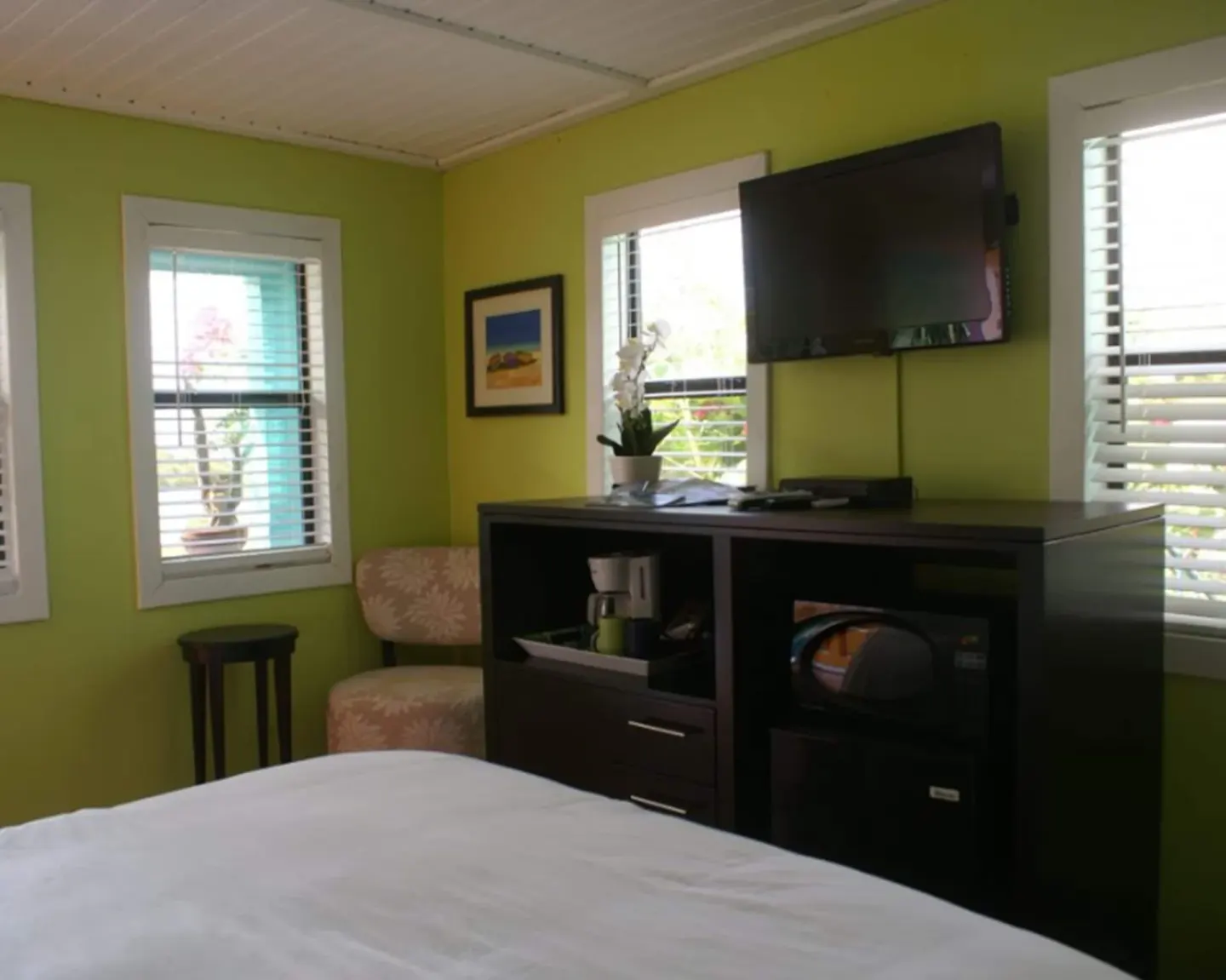 Standard Room bed area with wall-mounted TV, windows, chair, and cabinet at St John Inn.