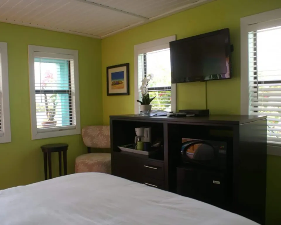 Standard Room bed area with wall-mounted TV, windows, chair, and cabinet at St John Inn.