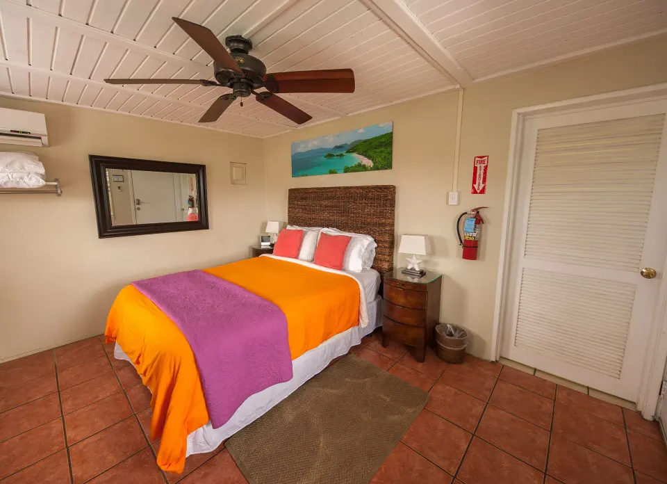 Standard Room bed with orange coverlet and purple throw at St John Inn.