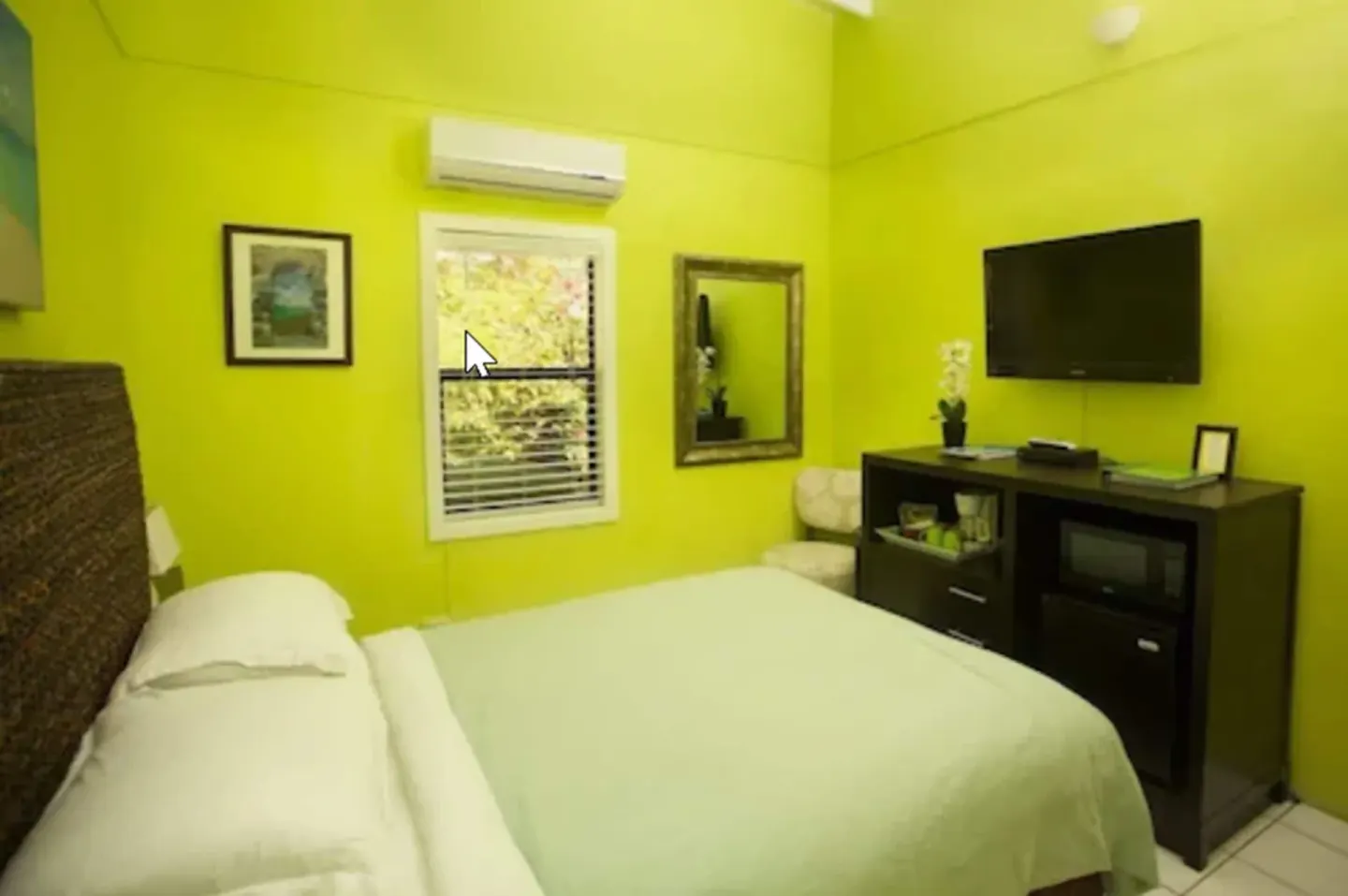 Standard Room bed with green walls, TV, mirror, and window at St John Inn.