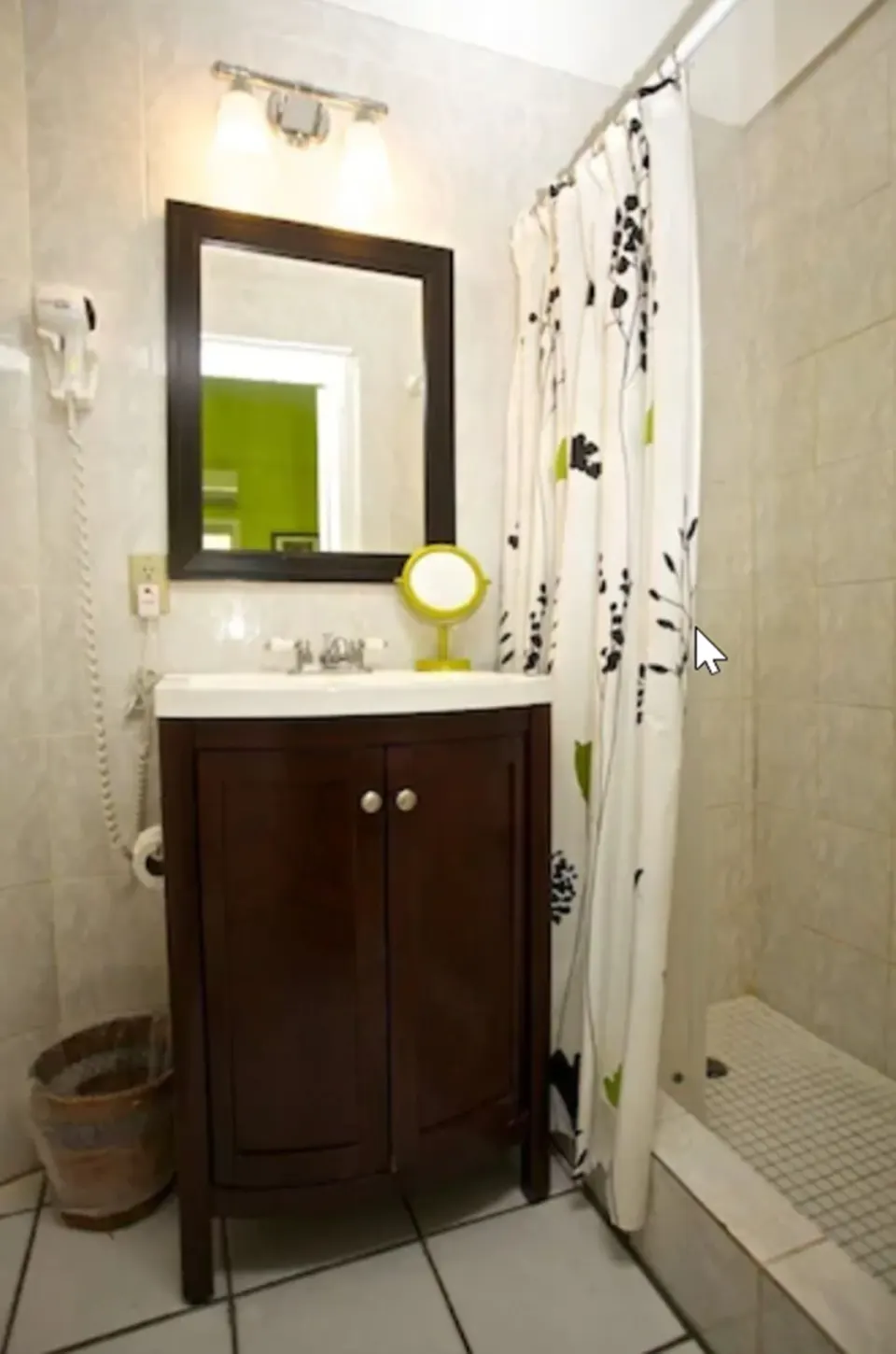 Standard Room bathroom at St John Inn with a vanity, mirror, shower curtain, tiled shower, and wall light.