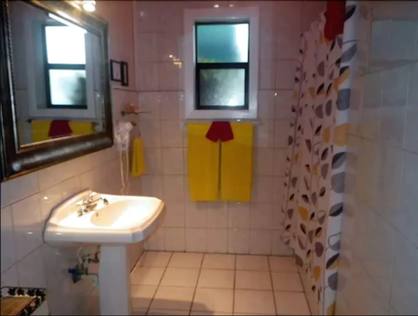 Suite bathroom with pedestal sink, mirror, window, towels, and shower curtain at St John Inn.