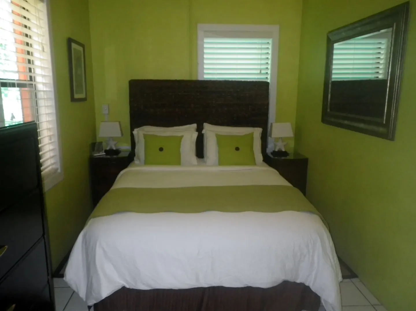 Suite bedroom with bed, green walls, shutters, and mirror at St John Inn.