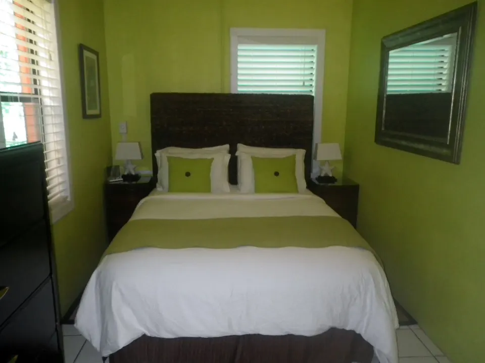 Suite bedroom with bed, green walls, shutters, and mirror at St John Inn.