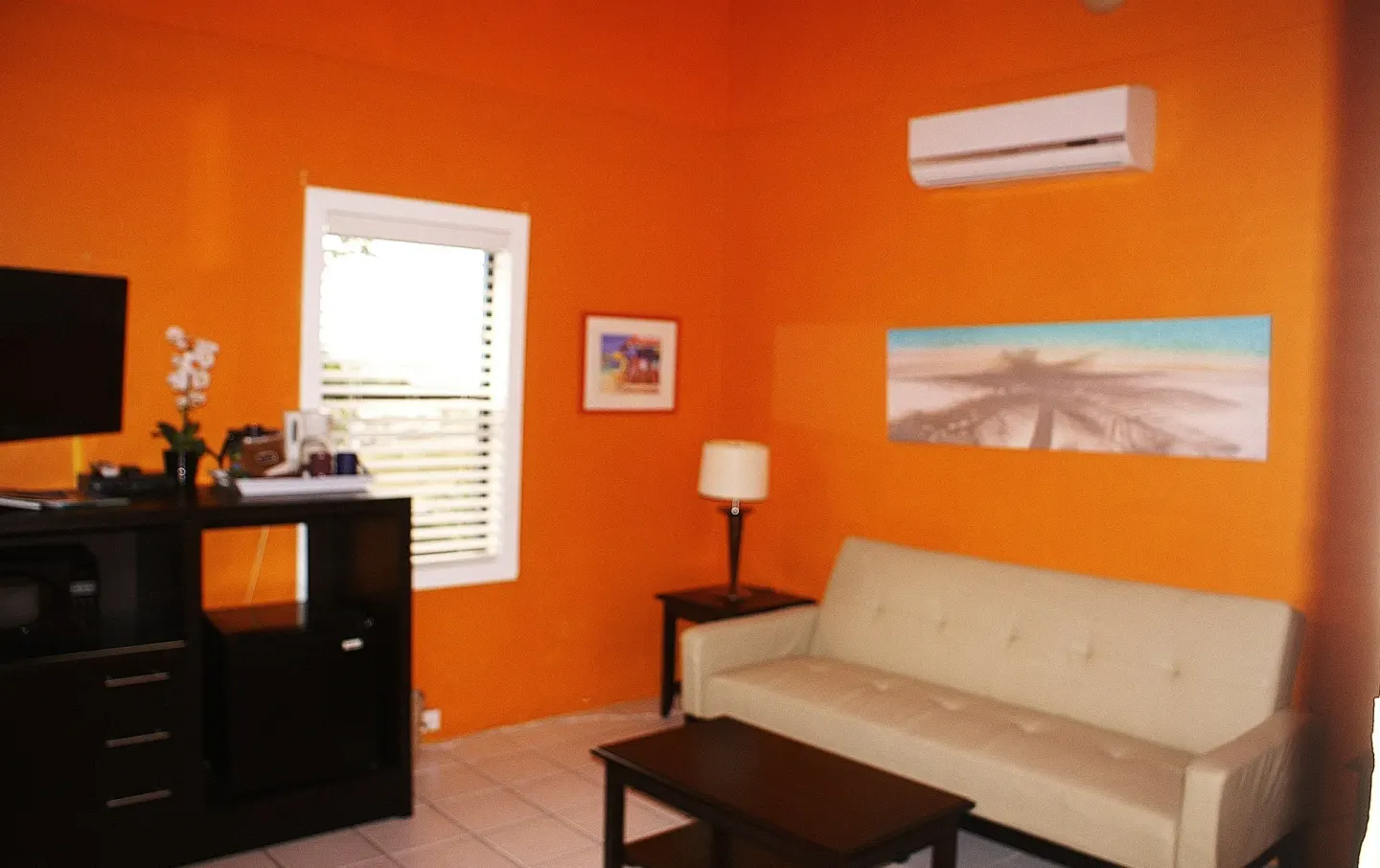 Suite sitting area with sofa bed, coffee table, TV, and orange wall at St John Inn.