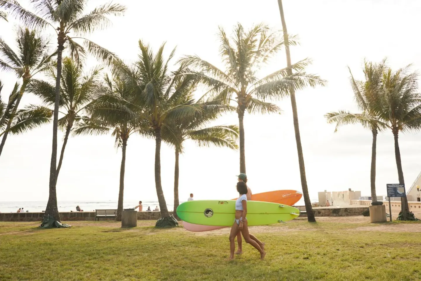 People carrying surfboards beneath palm trees near the beach by Stay Hotel Waikiki.