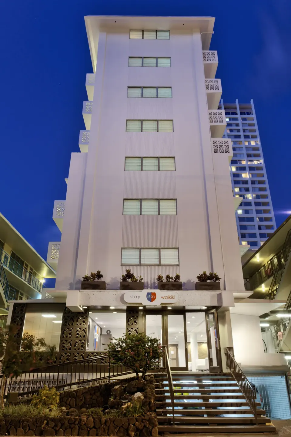The Stay Hotel Waikiki building and front steps are lit in the evening.
