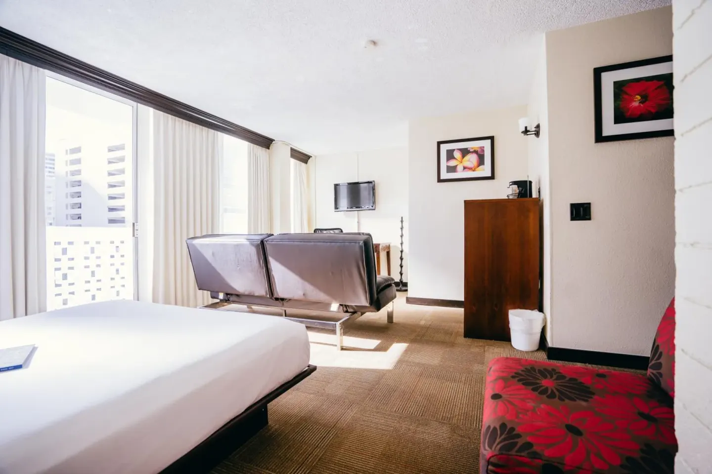 Guest room with white bed, sofa, TV, and tall windows at Stay Hotel Waikiki.