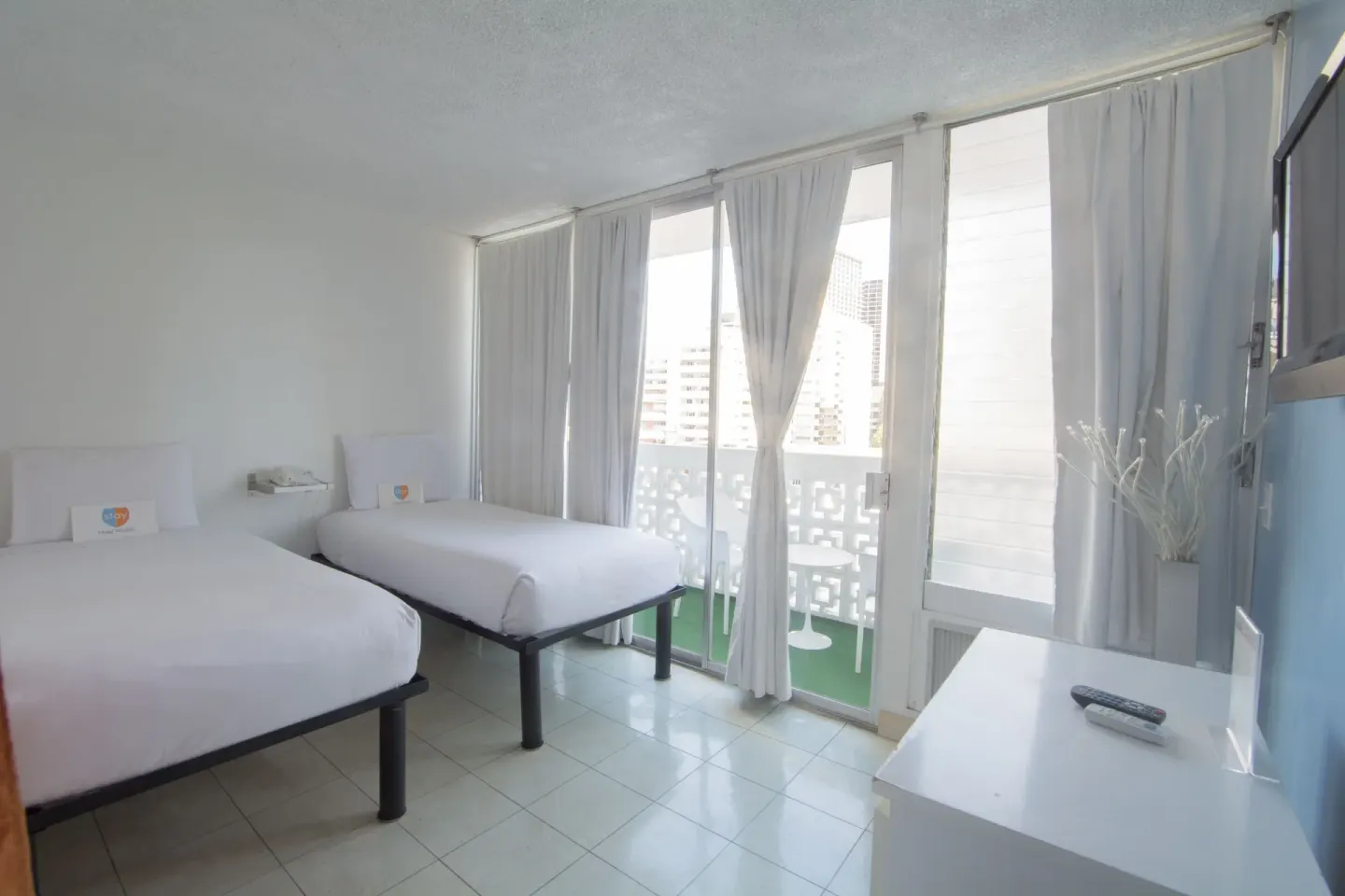 Two twin beds beside balcony windows and a dresser in a guest room at Stay Hotel Waikiki.