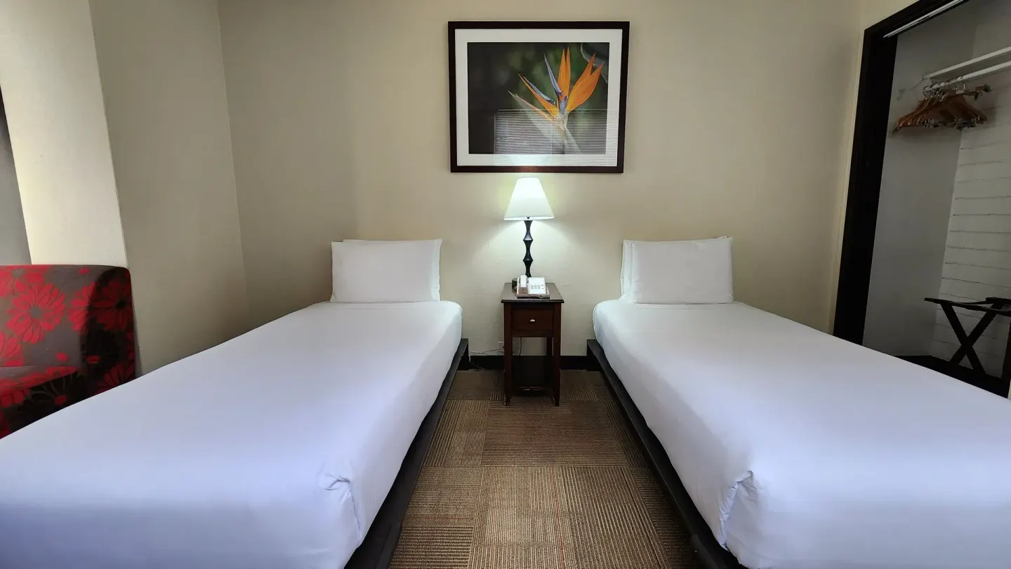 Two twin beds separated by a lit nightstand in a guest room at Stay Hotel Waikiki.