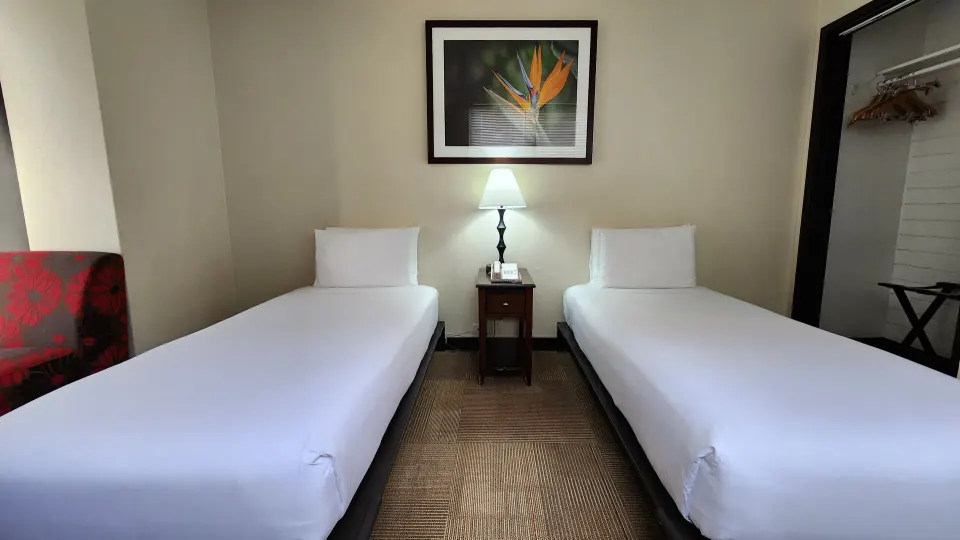 Two twin beds separated by a lit nightstand in a guest room at Stay Hotel Waikiki.