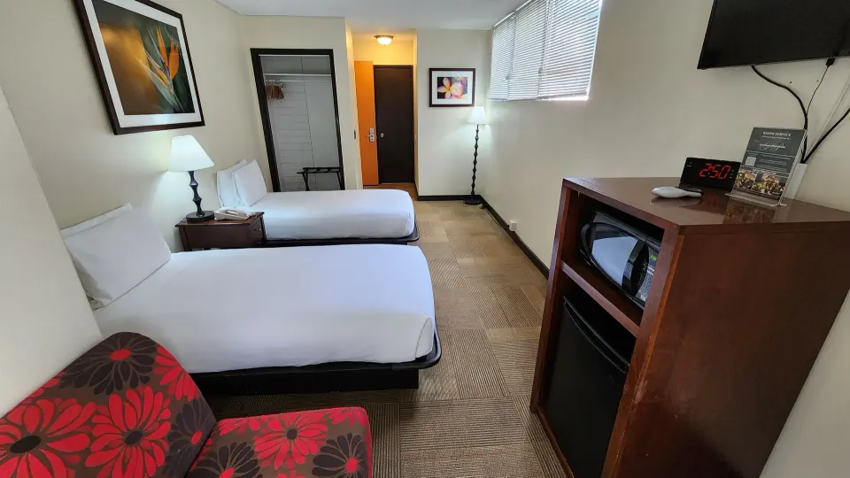 Two twin beds with a floral chair, TV, microwave, and mini fridge at Stay Hotel Waikiki.