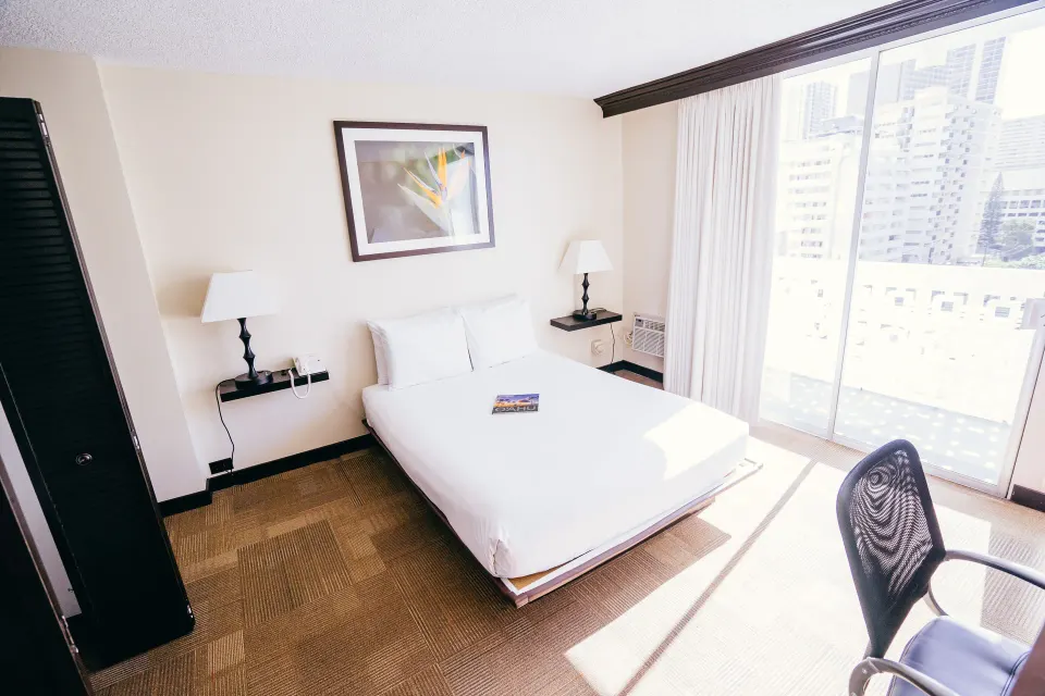 Boutique Room queen bed beside bright sliding glass doors at Stay Hotel Waikiki.