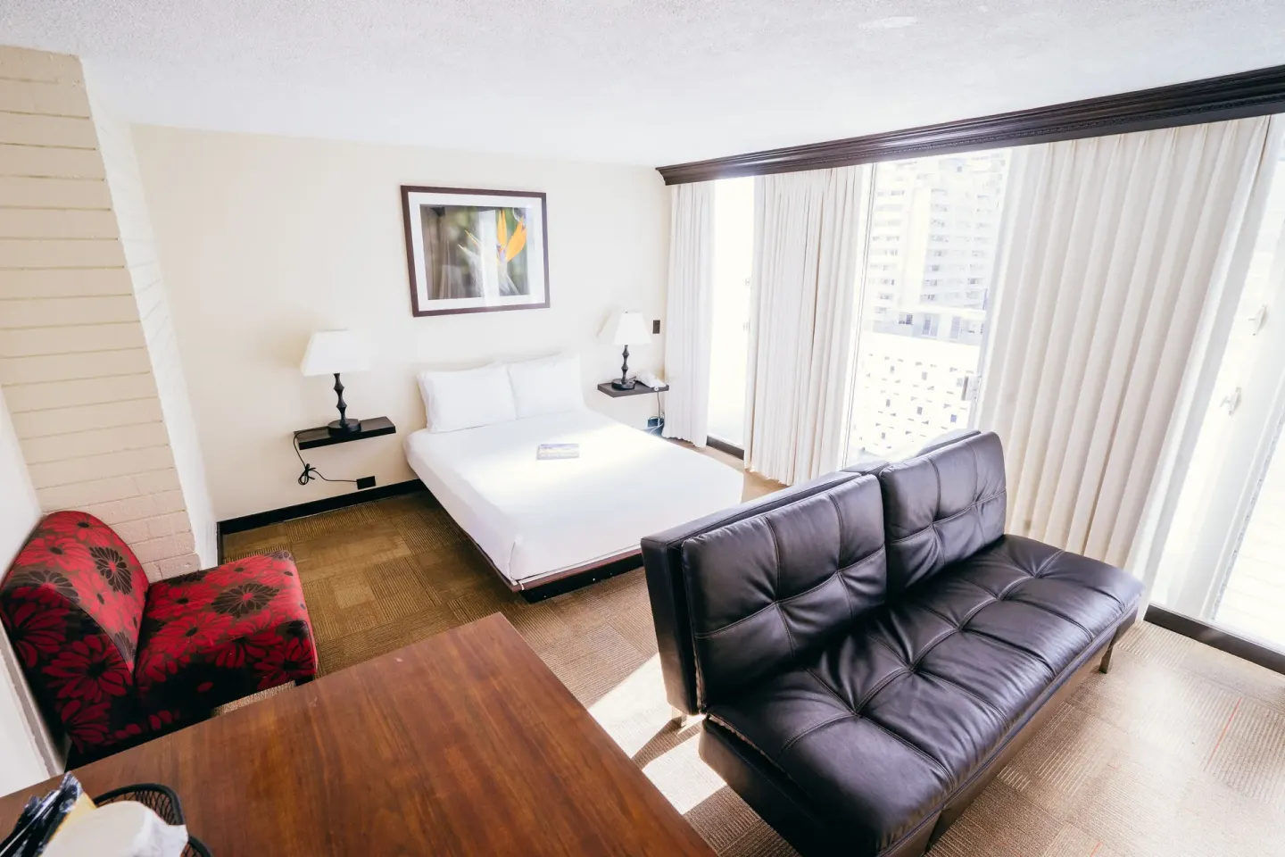 Deluxe Room with sofa bed and king bed at Stay Hotel Waikiki beside bright balcony windows.