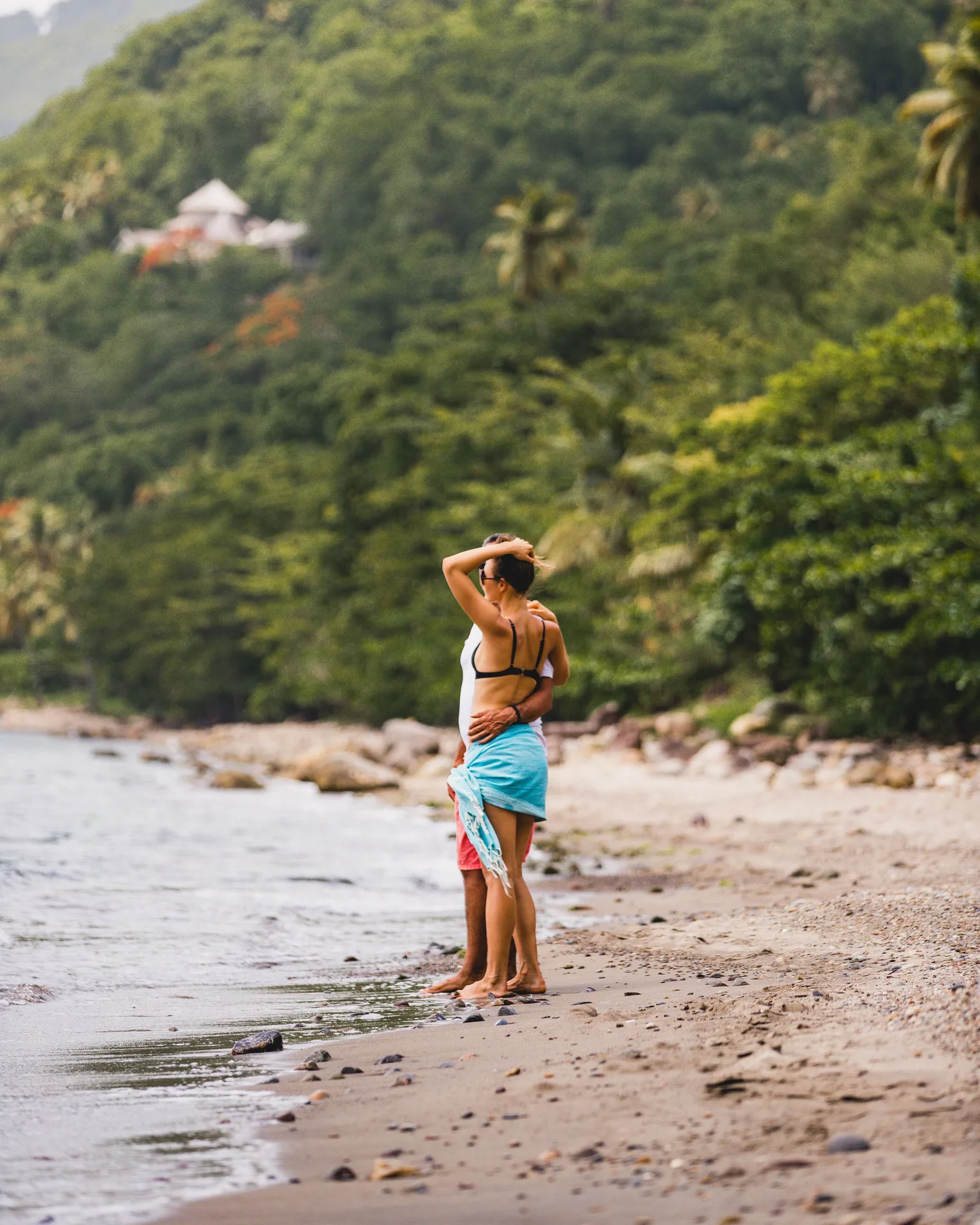 Couple standing at the shoreline near Stonefield Villa Resort with tropical greenery behind.