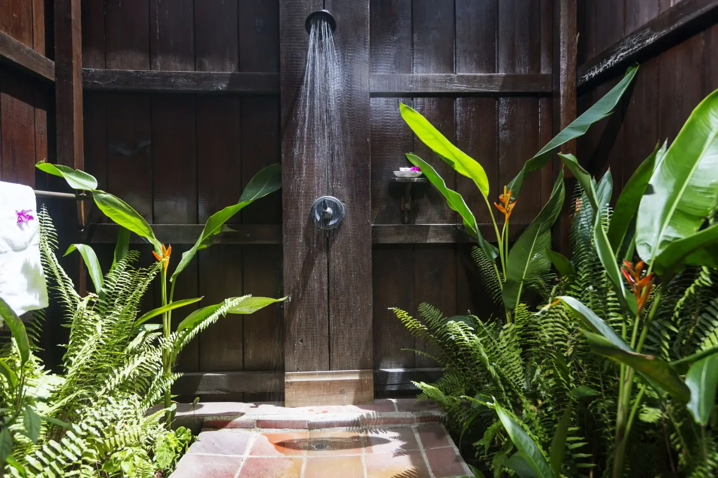 Outdoor shower with wood walls and tropical plants at Stonefield Villa Resort.