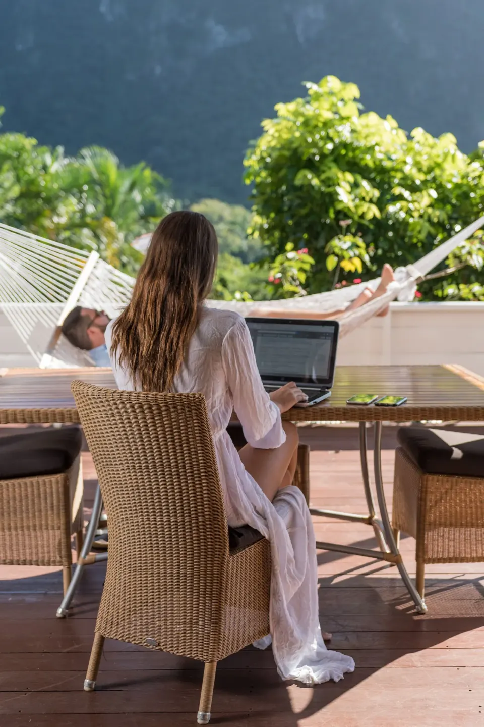 Guest using a laptop on a sunny deck beside a hammock at Stonefield Villa Resort.