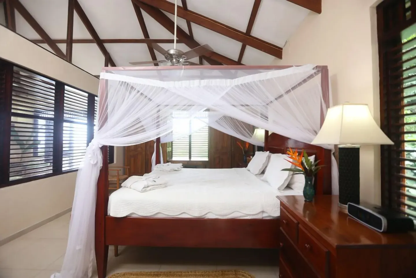 Canopy bed with dresser, lamp, and louvered windows at Stonefield Villa Resort.