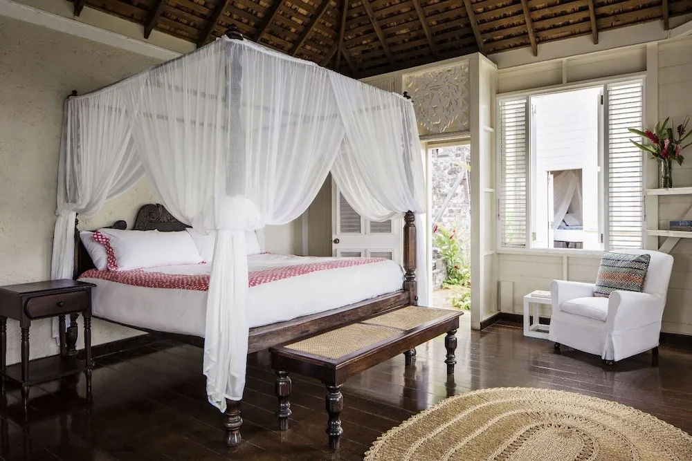 Guest room with four-poster canopy bed and white armchair at Strawberry Hill.