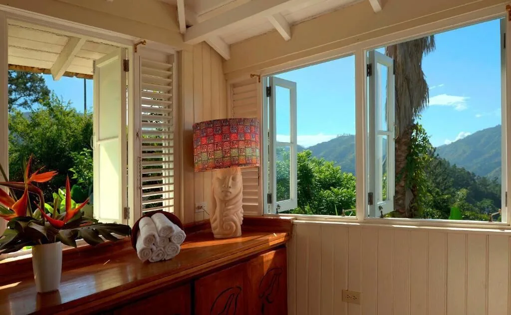 An airy room at Strawberry Hill has open windows, a dresser, towels, and mountain views.