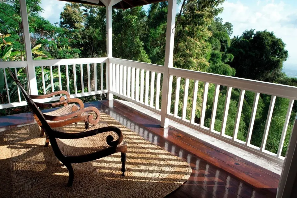 A Cottage 2 Bedrooms veranda at Strawberry Hill with lounge chairs, white railings, and tropical trees.