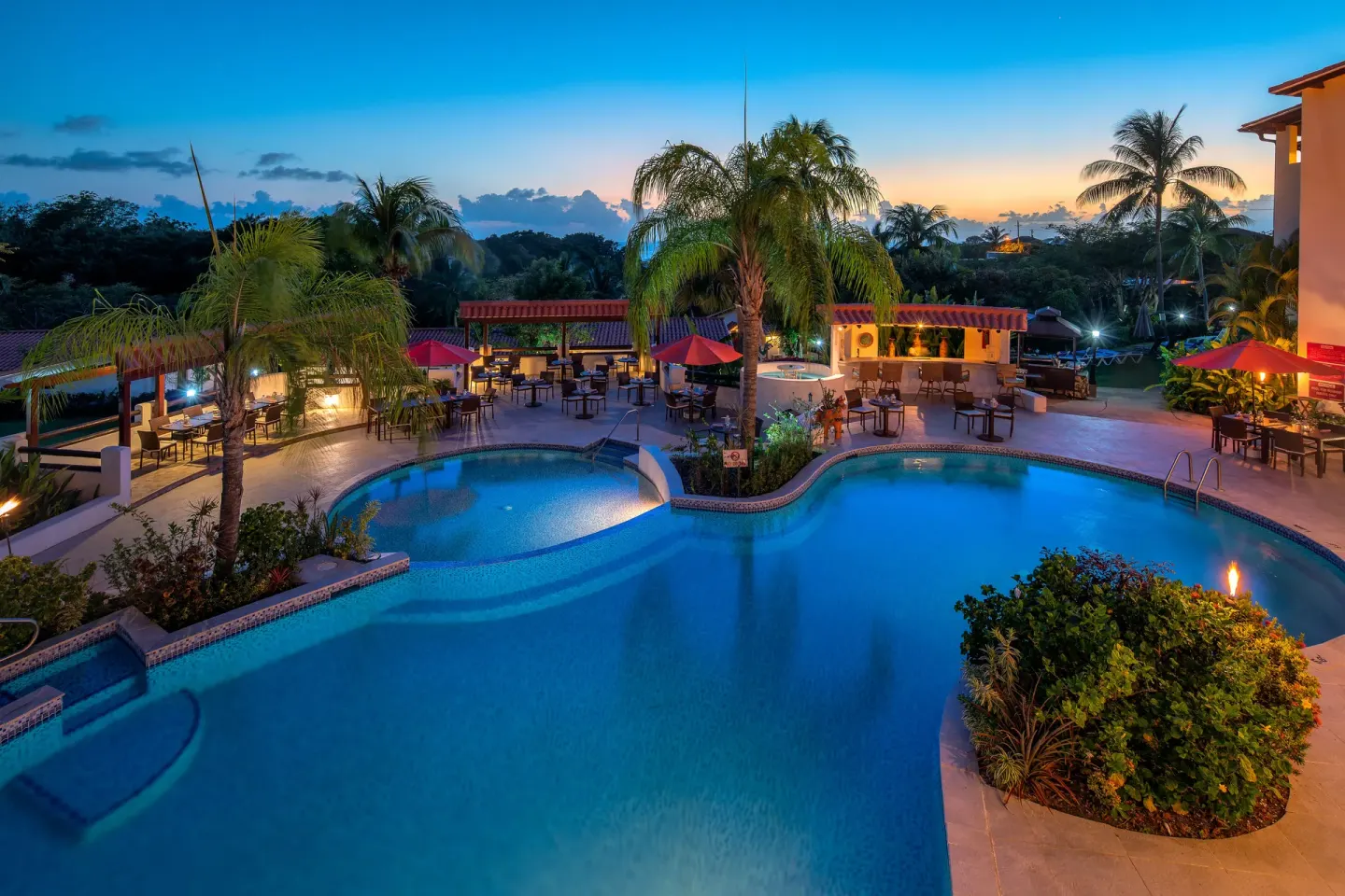 Evening pool deck with lit seating areas and bar at Sugar Cane Club Hotel And Spa.