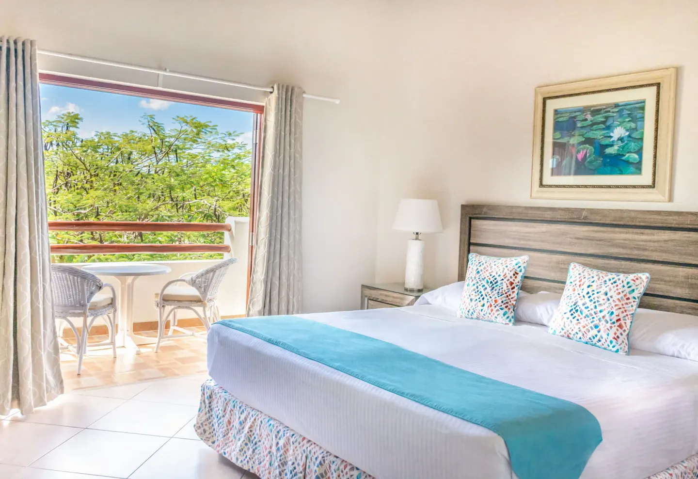 A bright guest room with a king bed and balcony seating at Sugar Cane Club Hotel And Spa.