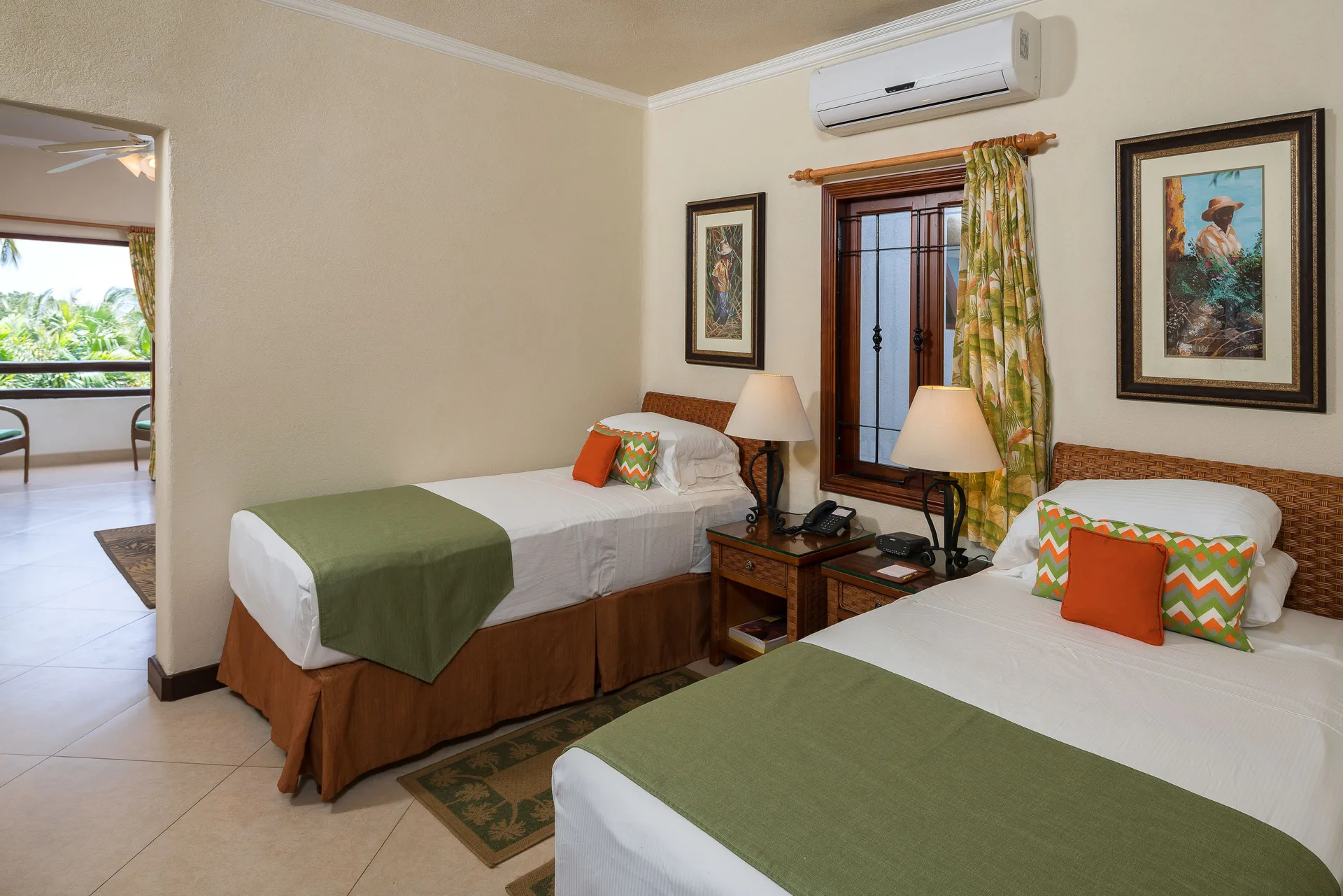 Guest room with two twin beds, bedside lamps, and balcony opening at Sugar Cane Club Hotel And Spa.