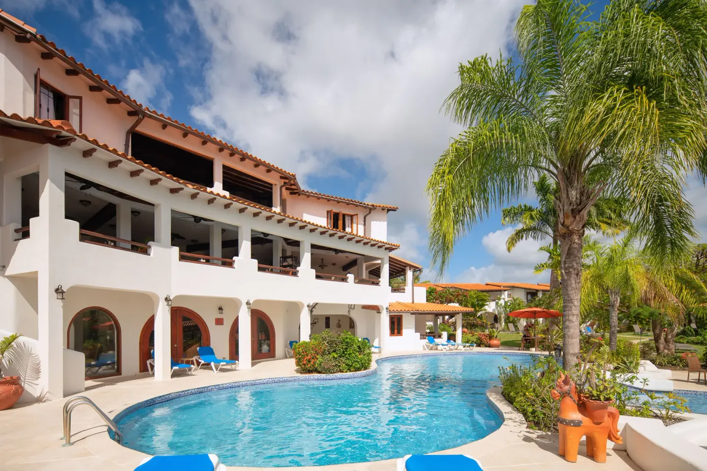 Curved pool beside white resort buildings and palm trees at Sugar Cane Club Hotel And Spa.