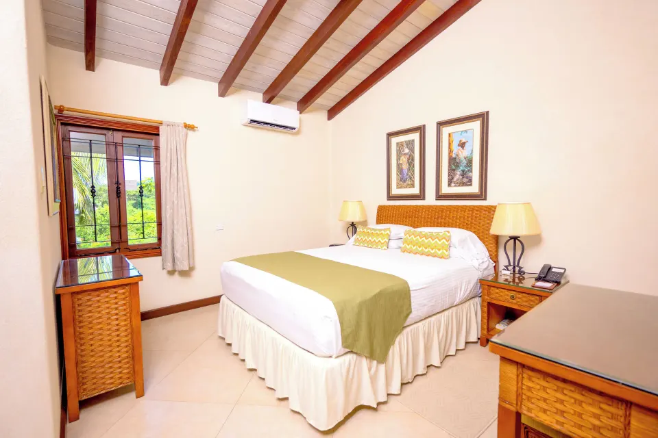 Suite bedroom with king bed, wicker furniture and window view at Sugar Cane Club Hotel And Spa.