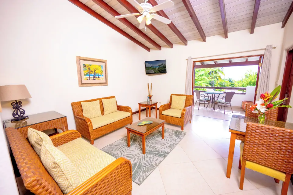 Suite living room with wicker sofas, dining table and balcony at Sugar Cane Club Hotel And Spa.