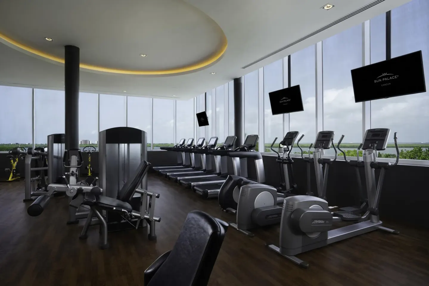 Fitness center with treadmills and cardio machines by tall windows at Sun Palace Cancun.