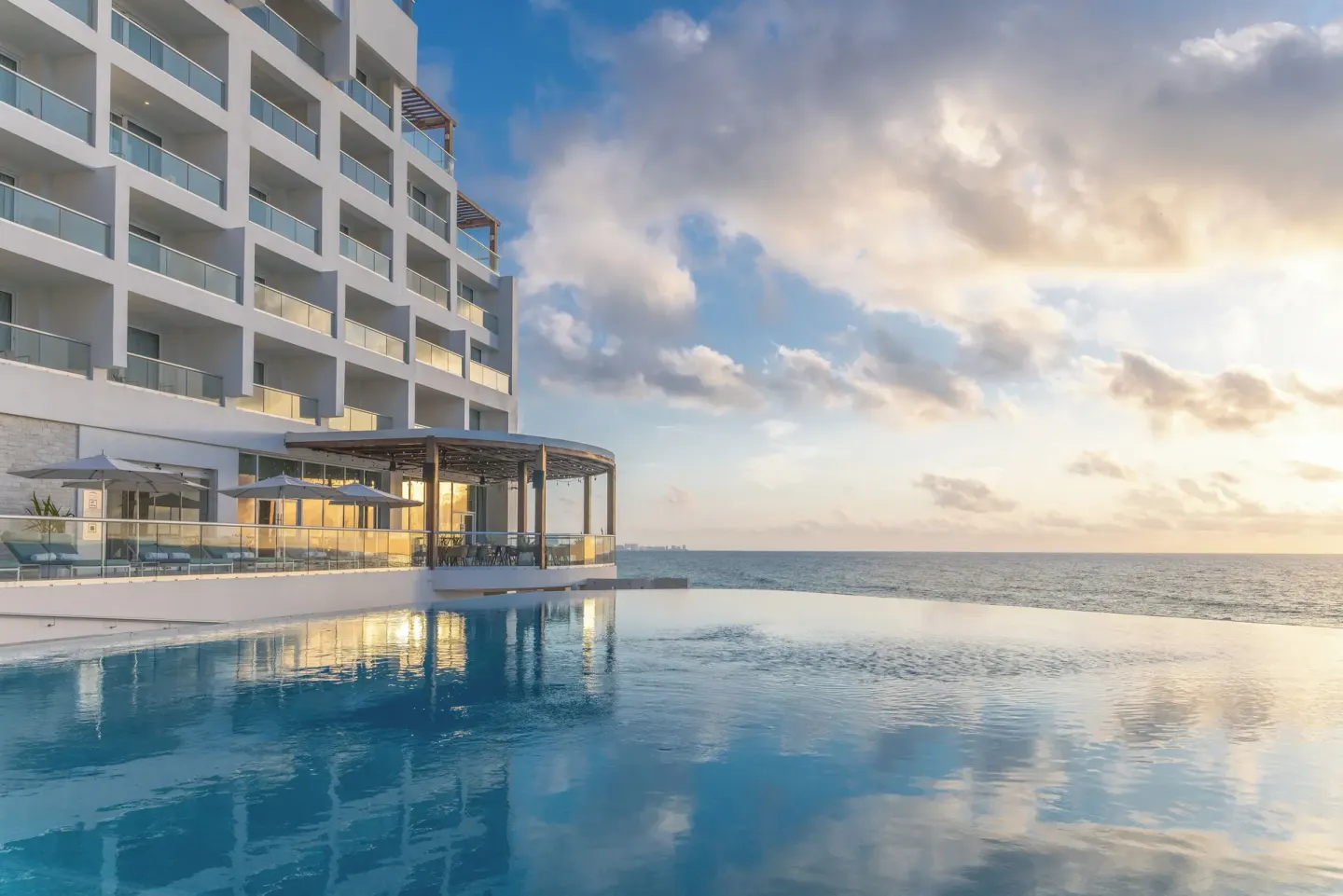 Infinity pool and oceanfront tower at Sun Palace Cancun under a cloudy sunset sky.