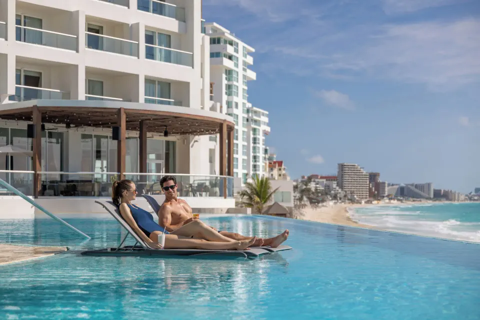 Guests recline on pool loungers overlooking the Cancun shoreline at Sun Palace Cancun.